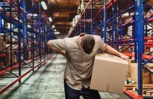 A man holding his back in pain after lifting heavy boxes at work.